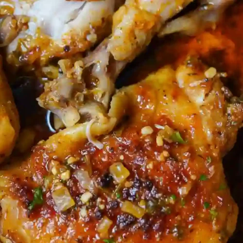Close-up of baked lemon butter chicken thighs, golden and garnished with minced garlic and herbs, showcasing a rich, savory sauce.