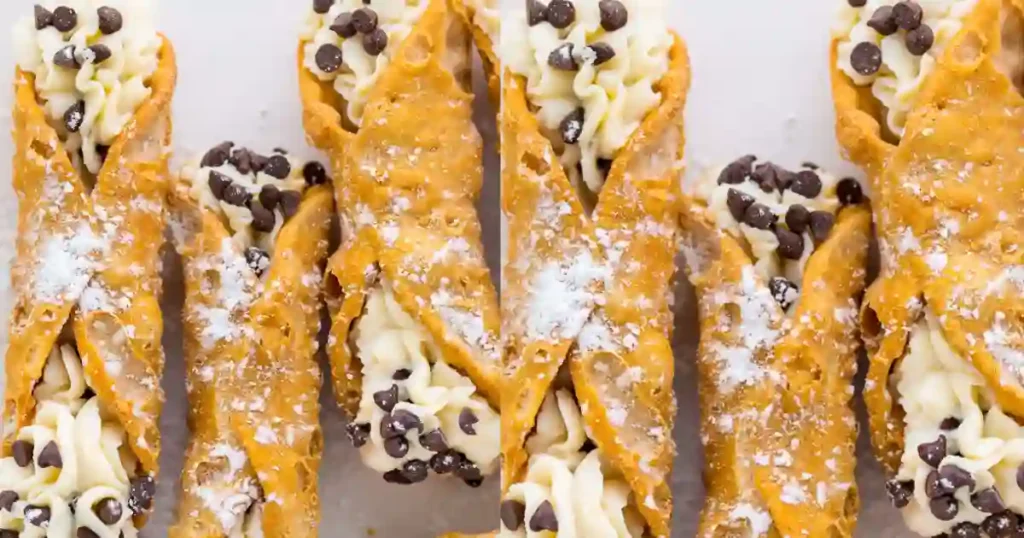 A close-up view of multiple golden-brown cannoli shells filled with a creamy, silky cannoli filling. The filling is adorned with mini chocolate chips and dusted with powdered sugar, showcasing the beautifully flaky shells.