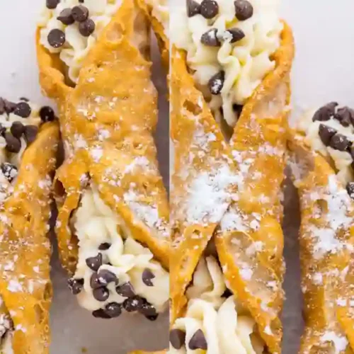 A close-up view of multiple golden-brown cannoli shells filled with a creamy, silky cannoli filling. The filling is adorned with mini chocolate chips and dusted with powdered sugar, showcasing the beautifully flaky shells.