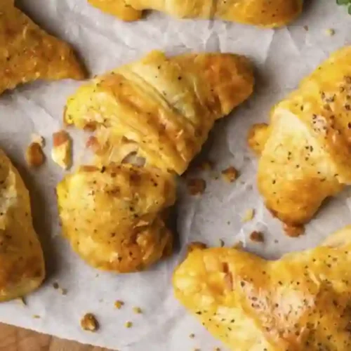 Golden, flaky crescent rolls filled with savory sausage, scrambled eggs, and melted cheese, fresh from the oven and lightly sprinkled with herbs.